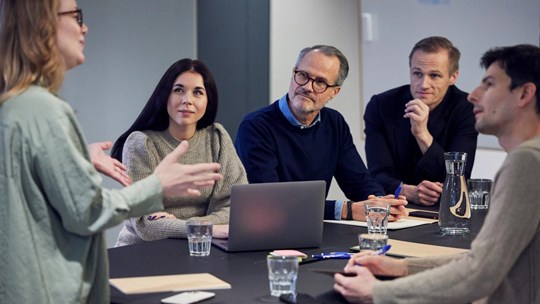 People in a meeting gathered listening to a woman present a speach